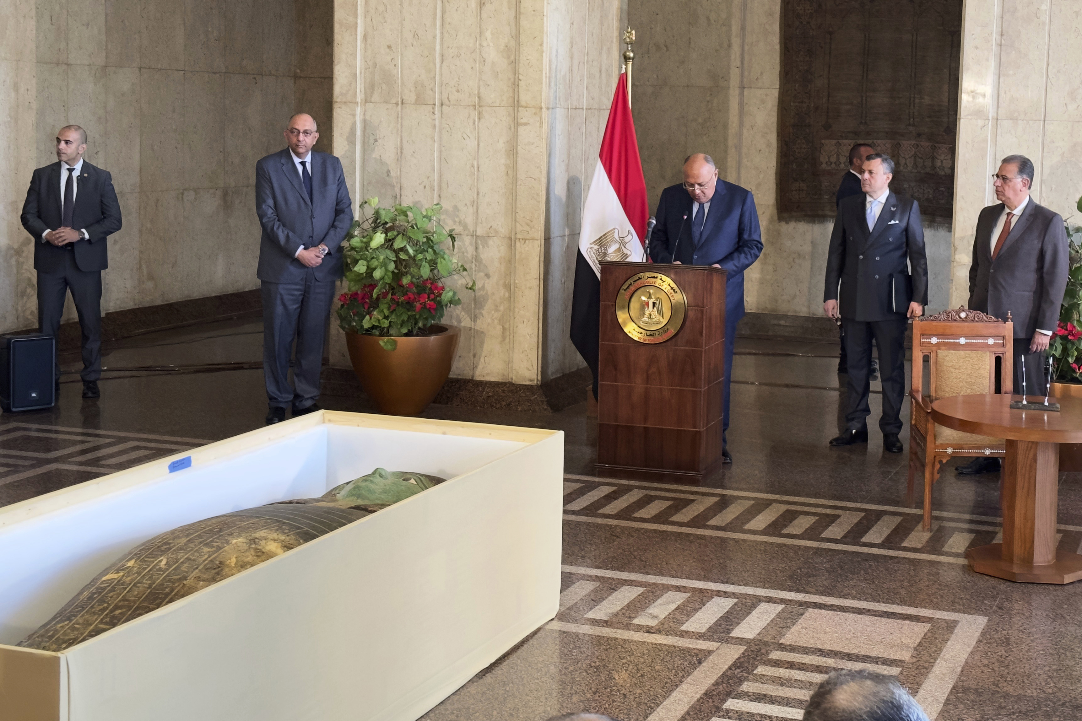 El ministro de Relaciones Exteriores, Sameh Shoukry, en el centro, de pie frente a un antiguo sarcófago de madera, habla durante una ceremonia de entrega en el Ministerio de Relaciones Exteriores en El Cairo, Egipto, el lunes 2 de enero de 2023. Un antiguo sarcófago de madera que se exhibió en el Museo de Houston de Natural Sciences fue devuelta a Egipto después de que las autoridades estadounidenses determinaran que fue saqueada hace años, dijeron funcionarios egipcios el lunes.  El ministro de Turismo y Antigüedades, Ahmed Issa, segundo a la derecha, escucha.  (Foto AP/Mohamed Salah)