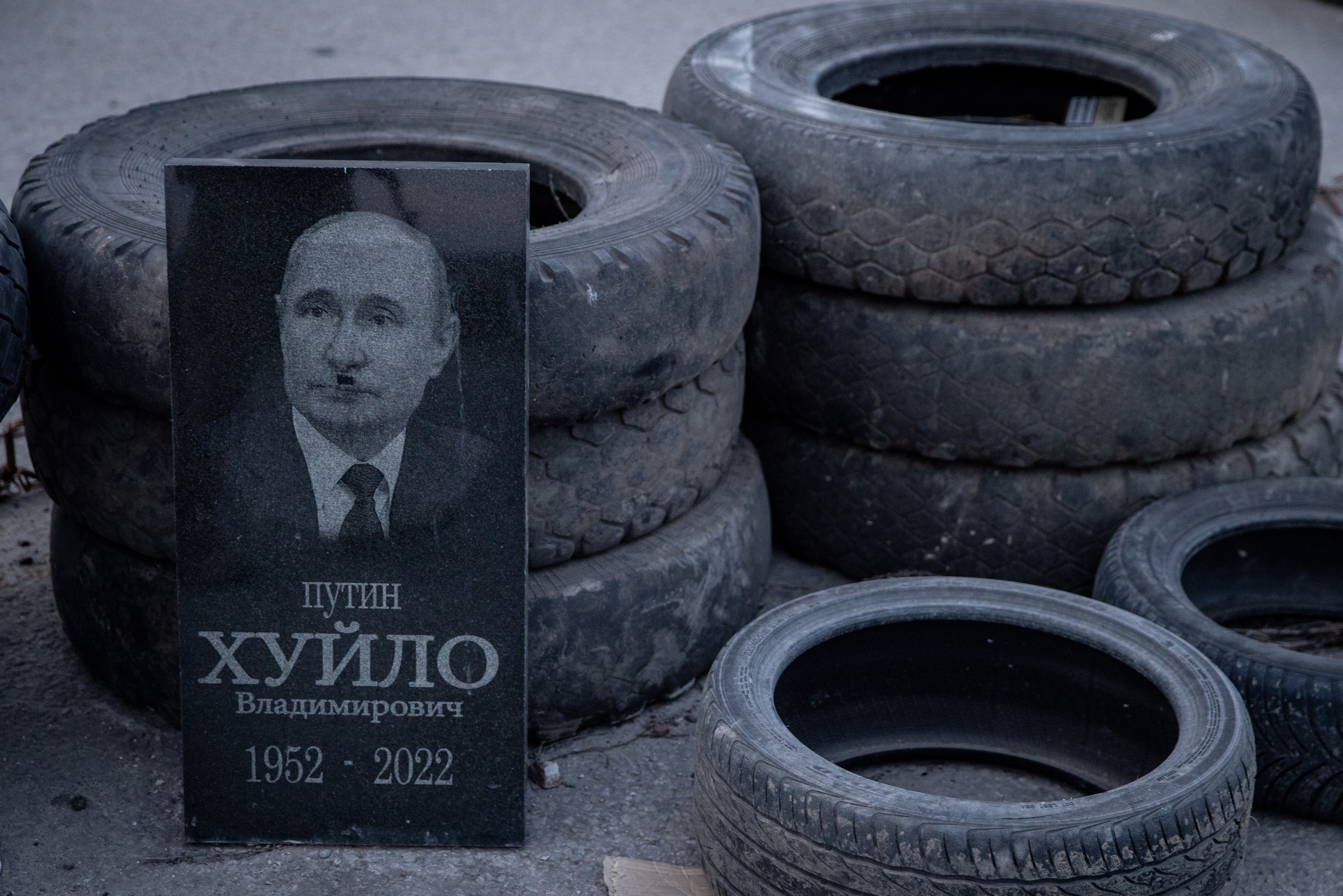 A grave stone showing the portrait of Russian President Vladimir Putin changed to look like Adolf Hitler is seen against a tyre barricade at a Ukrainian army checkpoint. 
