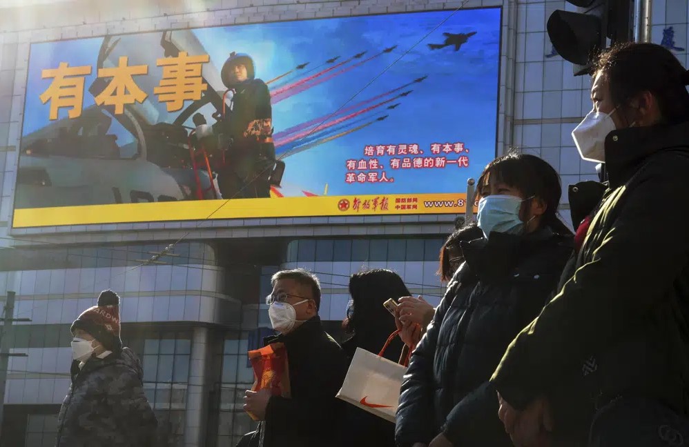 Residents wearing face masks wait to cross a traffic intersection near a large screen promoting the Chinese People's Liberation Army Airforce, in Beijing, Monday, Jan. 9, 2023. The Chinese military held large-scale joint combat strike drills starting Sunday, sending war planes and navy vessels toward Taiwan, both the Chinese and Taiwanese defense ministries said. (AP Photo/Andy Wong)