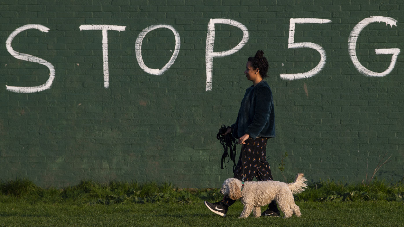 A woman in England walks past an anti-5G graffiti message.