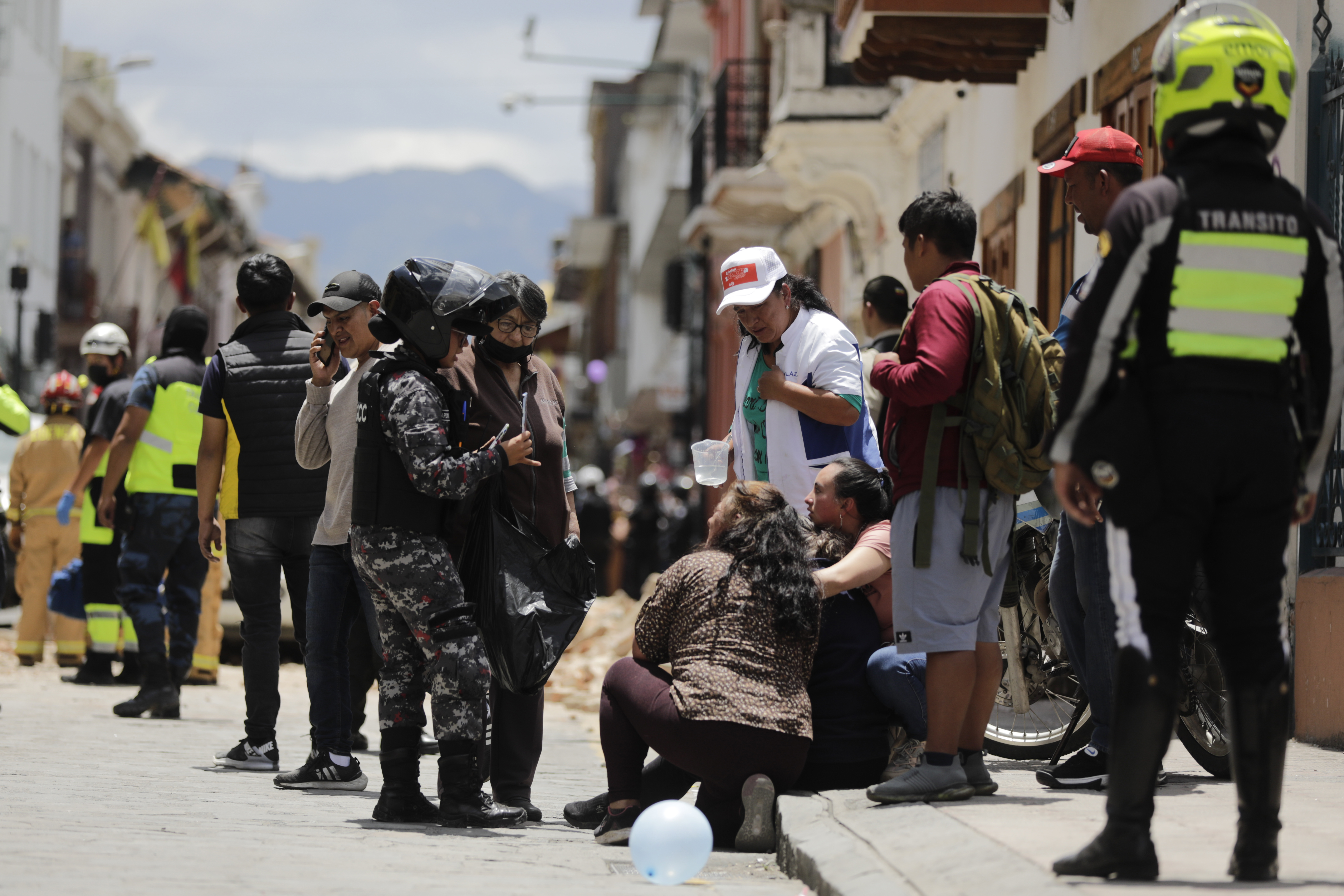 Police talks to people next to the site where a car was crushed by debris after an earthquake shook Cuenca, Ecuador, Saturday, March 18, 2023.